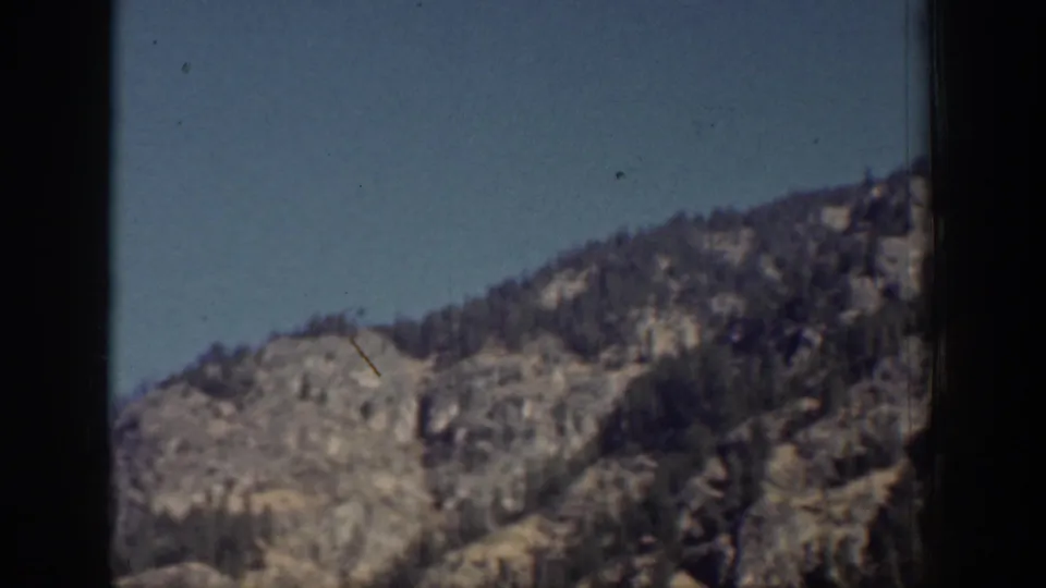 Vintage 8mm view of a Chelan-area rocky outcrop with scattered evergreens and open sky.