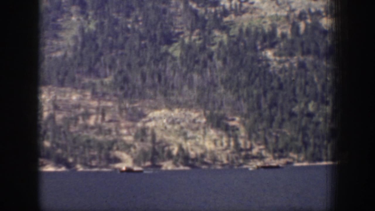 1939 Chelan, Washington 8mm frame showing a blue lake below evergreen and rocky mountain slopes, partly obscured by dark frame edges.