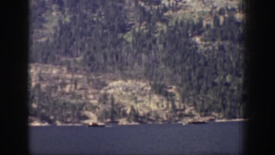1939 Chelan, Washington 8mm frame showing a blue lake below evergreen and rocky mountain slopes, partly obscured by dark frame edges.