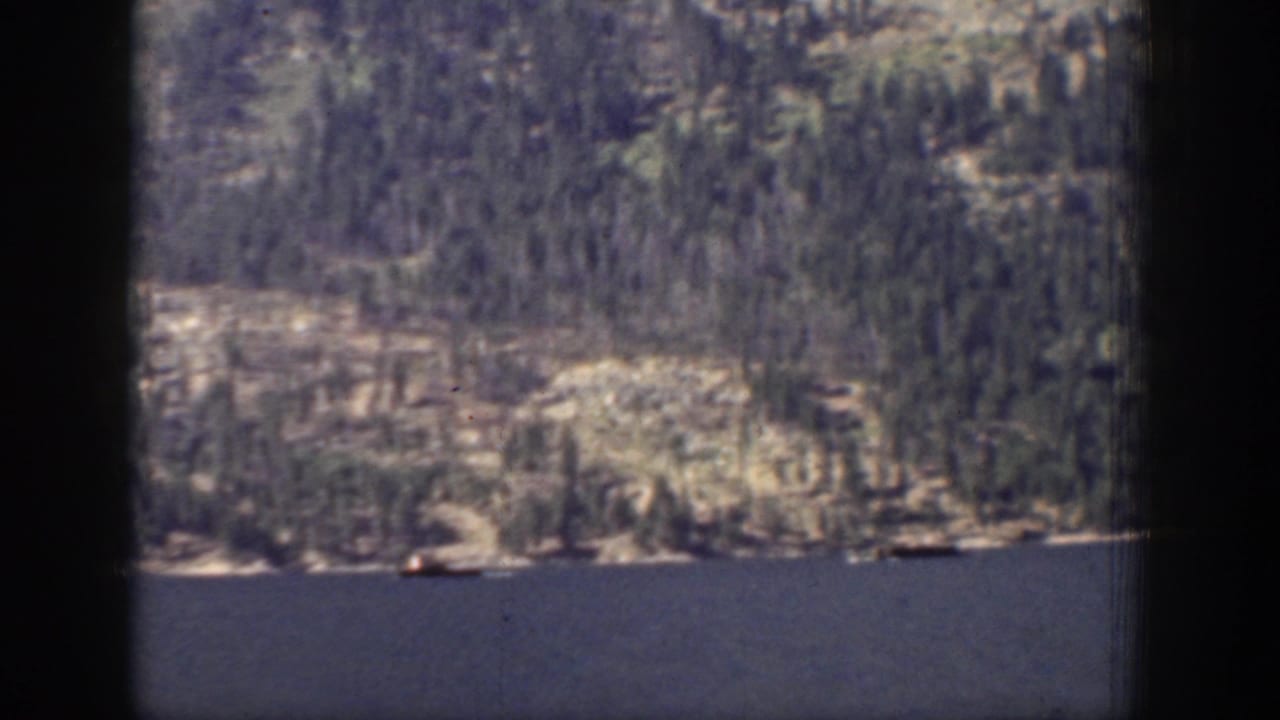 Forested rocky hillside above a dark blue lake with a small distant boat.