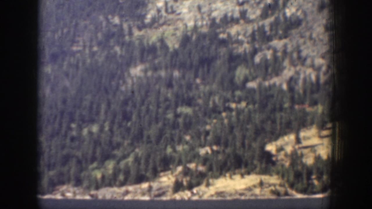 1939 Chelan, Washington 8mm frame showing a forested mountain slope and shoreline above blue lake water, partly bordered by dark frame edges.