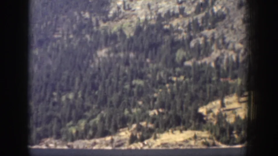 1939 Chelan, Washington 8mm frame showing a forested mountain slope and shoreline above blue lake water, partly bordered by dark frame edges.