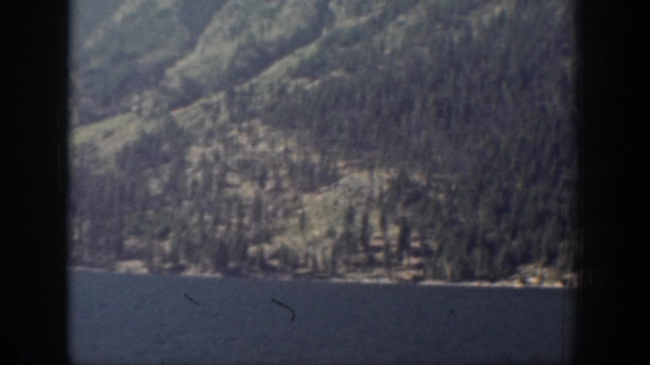 1939 Chelan, Washington 8mm frame showing blue lake water below a soft, shadowed forested mountain slope.
