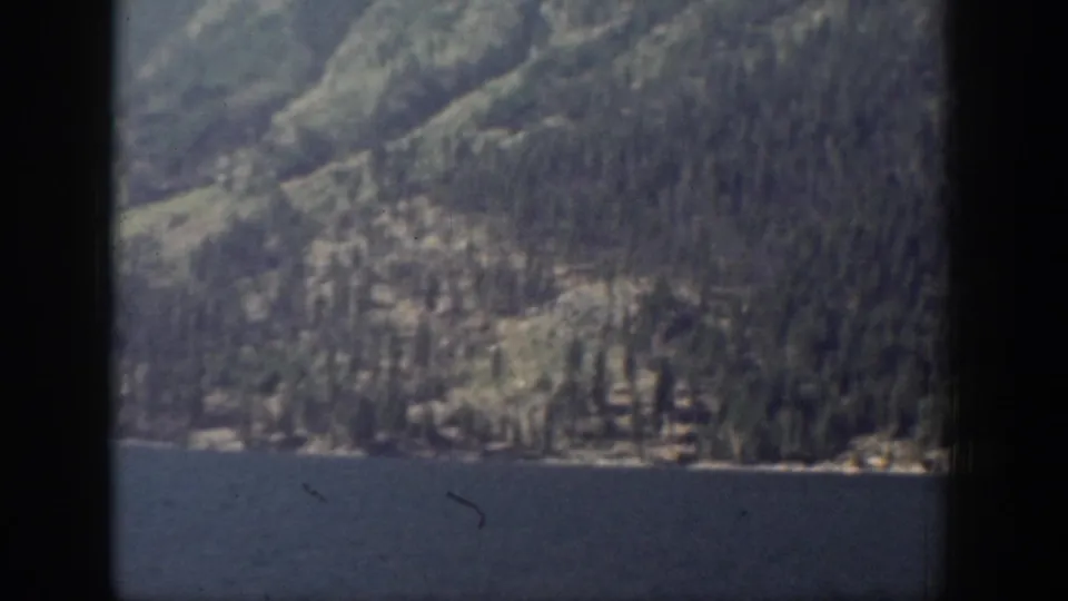1939 Chelan, Washington 8mm frame showing blue lake water below a soft, shadowed forested mountain slope.