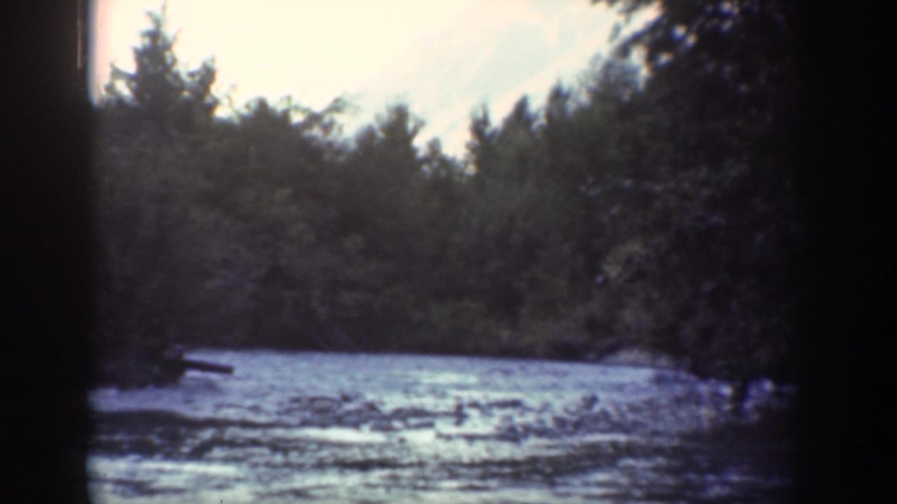 1939 Chelan, Washington home-movie frame showing a shallow river, wooded banks, pale sky, and dark film borders.