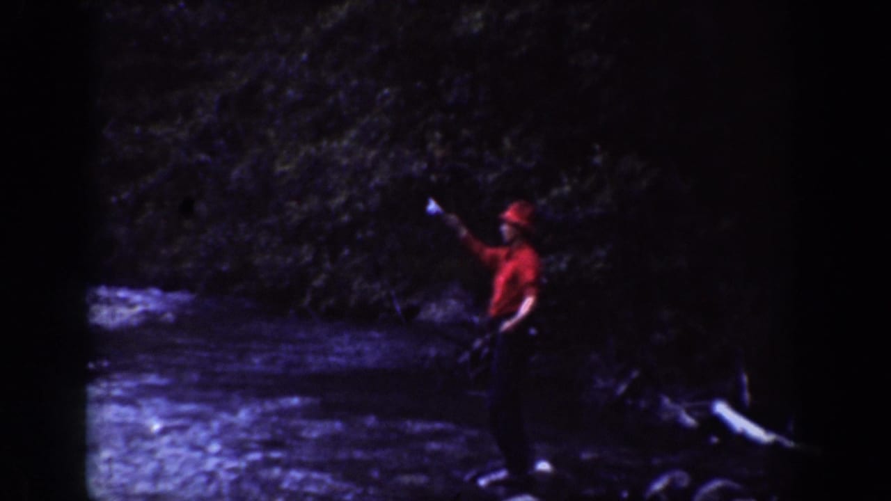 Chelan, Washington home-movie frame from 1939 showing a man in red raising a fishing line near a shallow forest river.