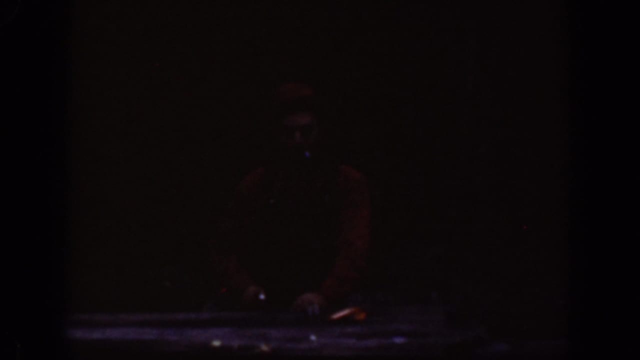 Underexposed 8mm frame from the Chelan footage with a barely visible adult figure standing near the river area.