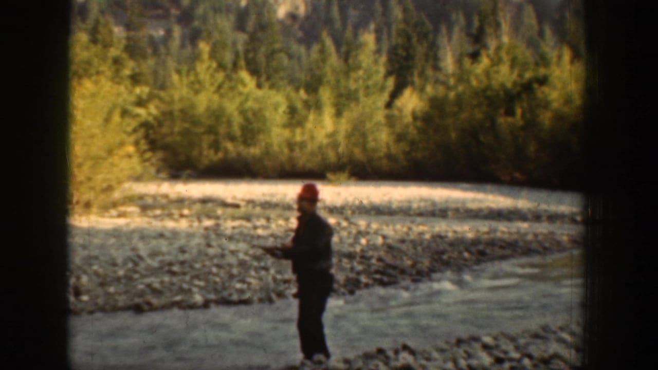 1939 Chelan, Washington 8mm frame showing a man in a red cap standing in shallow river water with forest behind him.