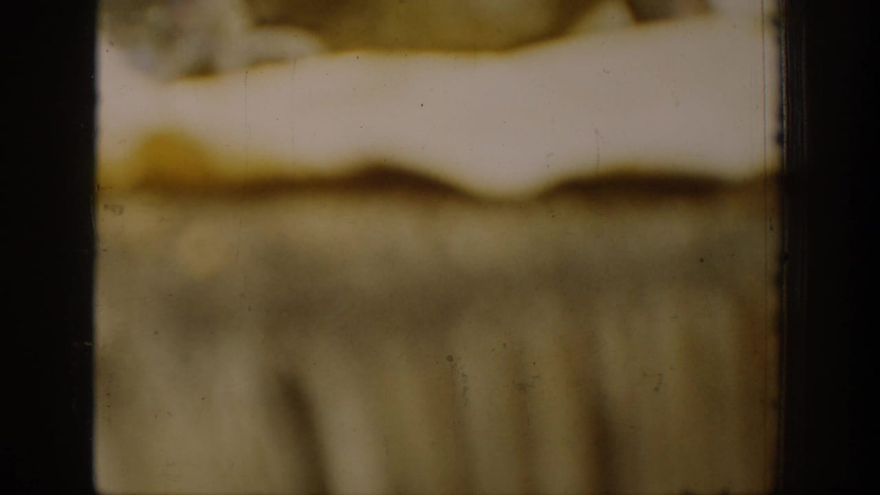 1939 Chelan 8mm frame fragment with soft yellow-brown emulsion, dark film edges, scratches, and an indistinct scene.