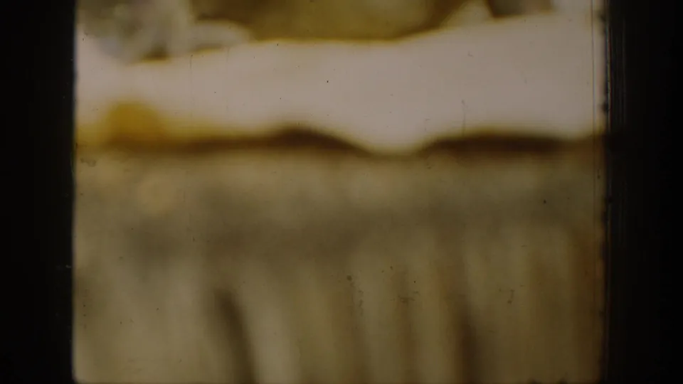 1939 Chelan 8mm frame fragment with soft yellow-brown emulsion, dark film edges, scratches, and an indistinct scene.