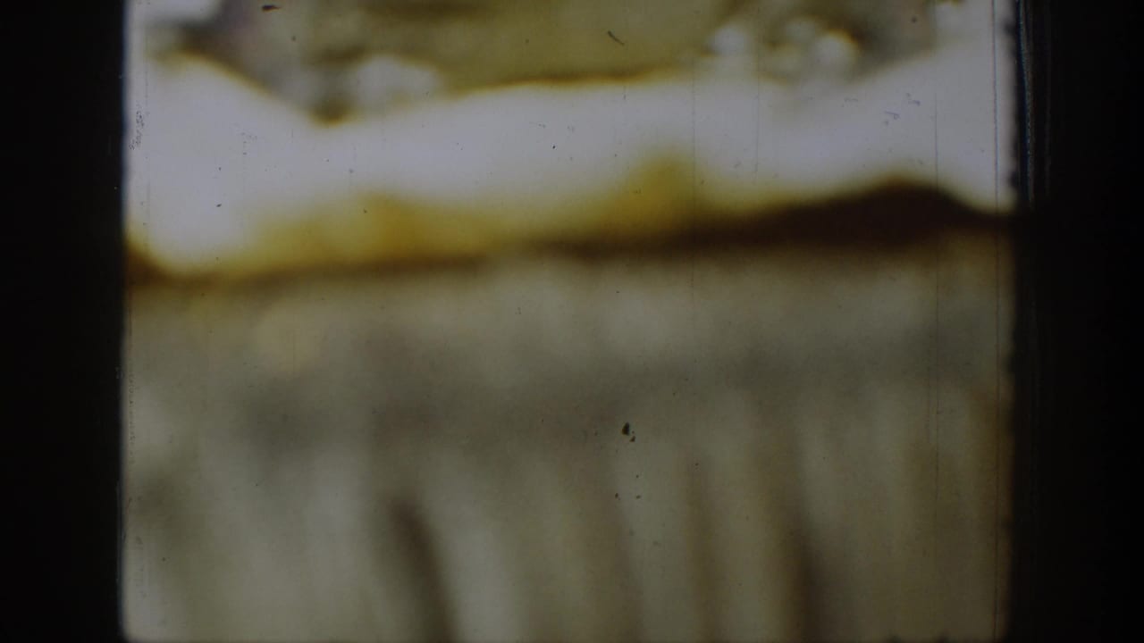 A 1939 Chelan 8mm frame with warped-looking edges, a dark central band, yellow-brown staining, and indistinct detail.