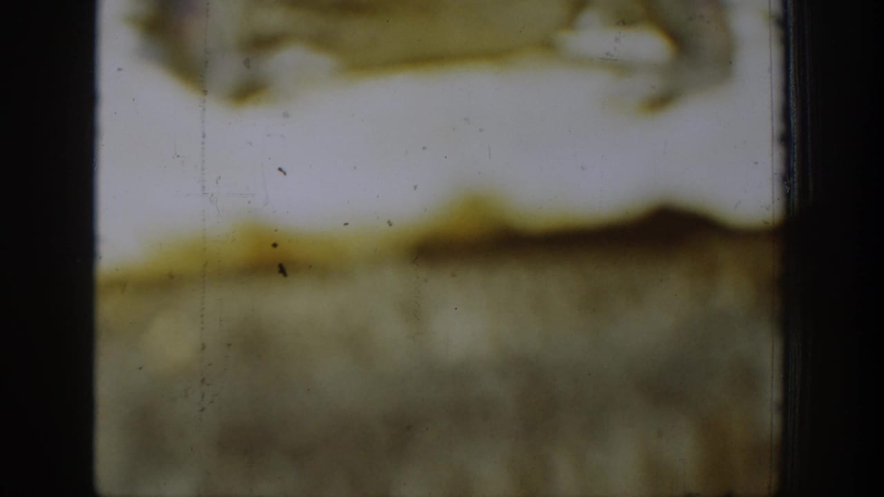 Final 1939 Chelan 8mm frame showing faded yellow emulsion, black frame edges, dust specks, scratches, and no identifiable people or property.