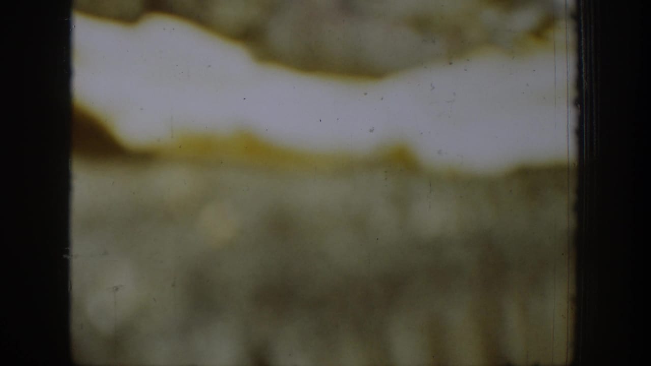Blurred 8mm frame with pale upper area, green lower band, and dark borders.