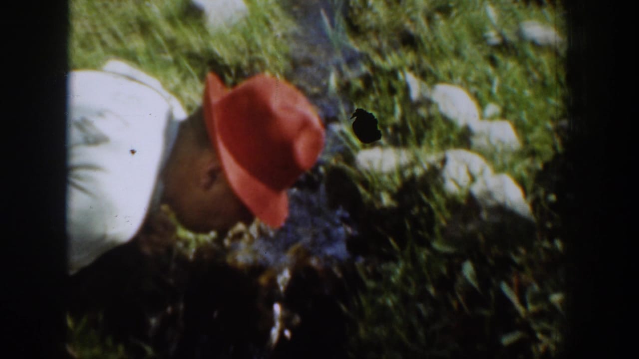 In 1939 Chelan home-movie footage, a man in a white shirt and red hat leans down beside a narrow grassy stream.