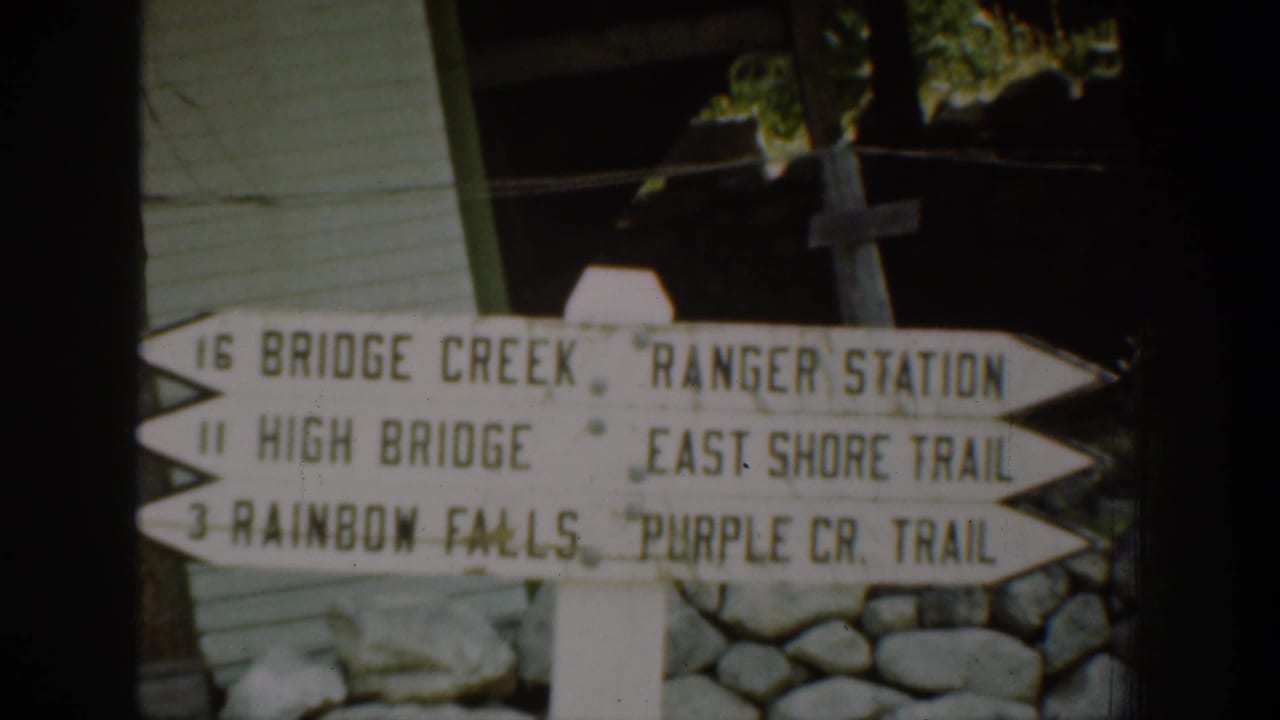 1939 Chelan-area frame with a wooden trail sign pointing toward Bridge Creek, High Bridge, Rainbow Falls, and nearby trails.
