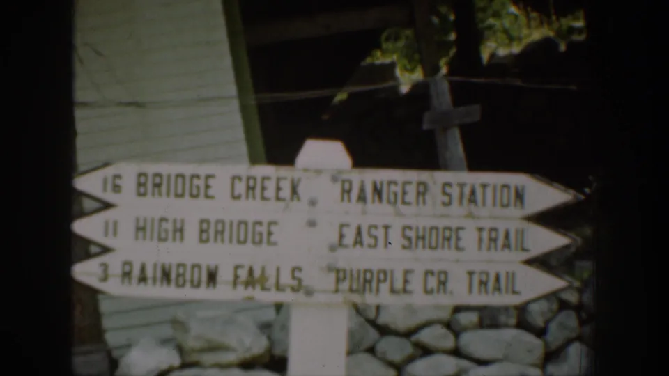 1939 Chelan-area frame with a wooden trail sign pointing toward Bridge Creek, High Bridge, Rainbow Falls, and nearby trails.
