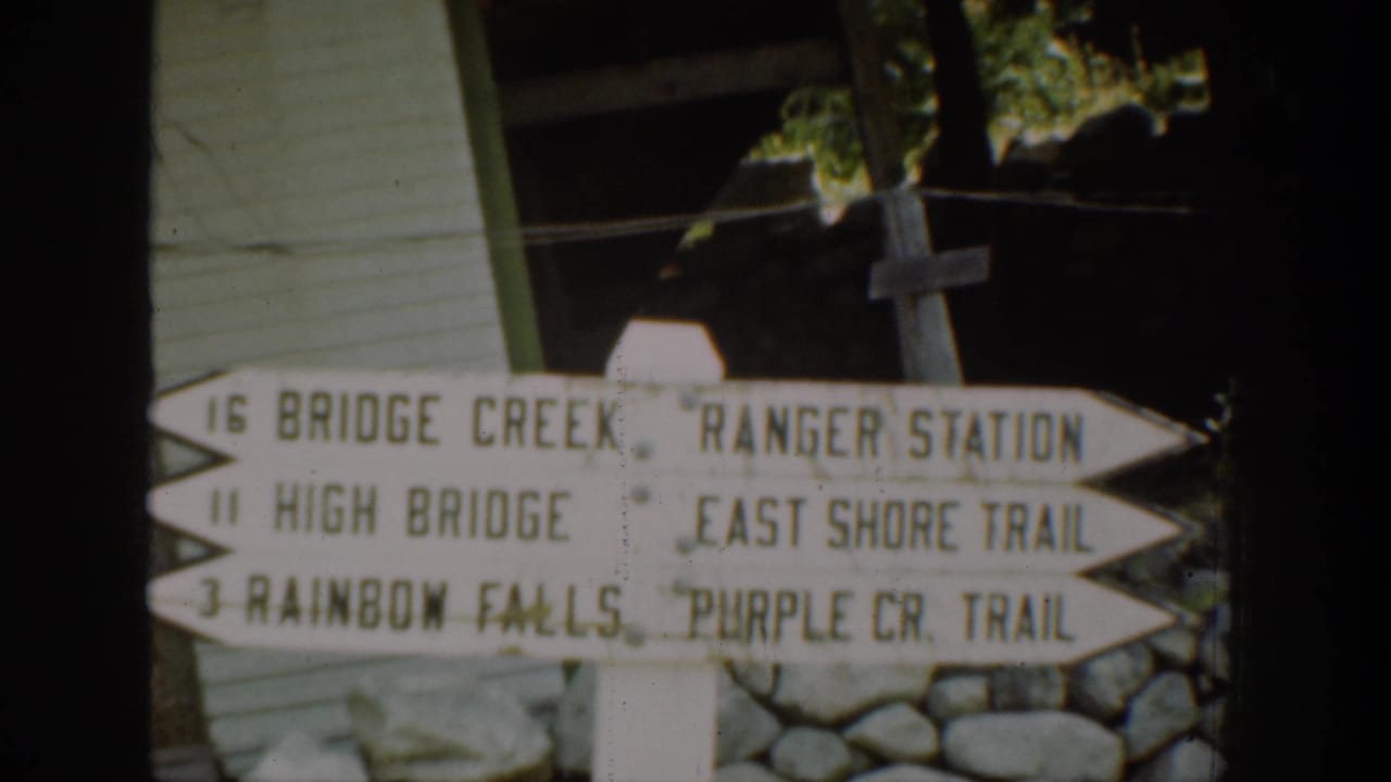 Chelan-area 8mm frame showing a directional trail sign for Bridge Creek, High Bridge, Rainbow Falls, Ranger Station, and East Shore Trail.