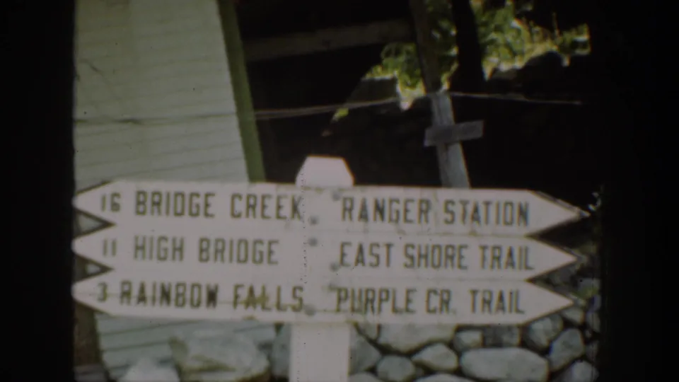Chelan-area 8mm frame showing a directional trail sign for Bridge Creek, High Bridge, Rainbow Falls, Ranger Station, and East Shore Trail.