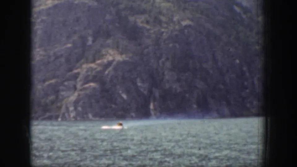 Distant swimmer in Chelan, Washington, seen on lake water against a rugged mountain backdrop in 1939 8mm footage.