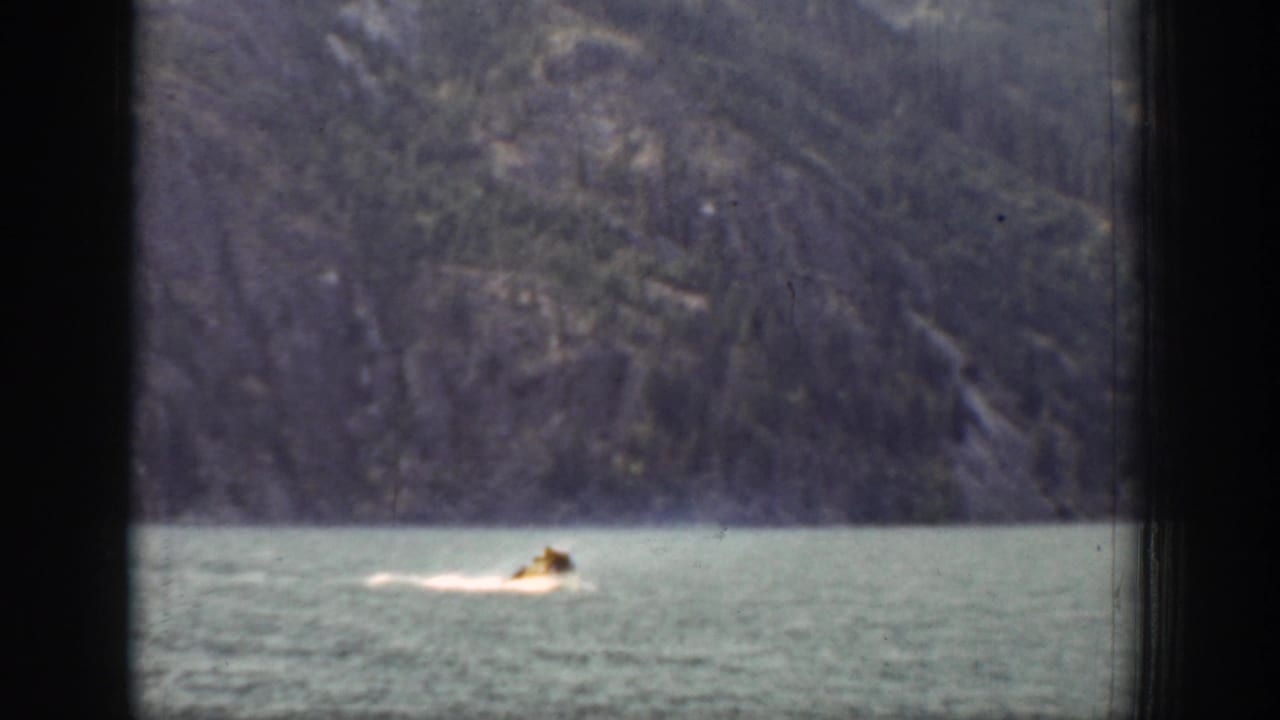 Late-1930s 8mm frame from Chelan showing a swimmer moving across open water below a rugged mountain slope.