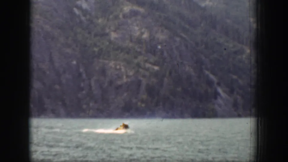 Late-1930s 8mm frame from Chelan showing a swimmer moving across open water below a rugged mountain slope.