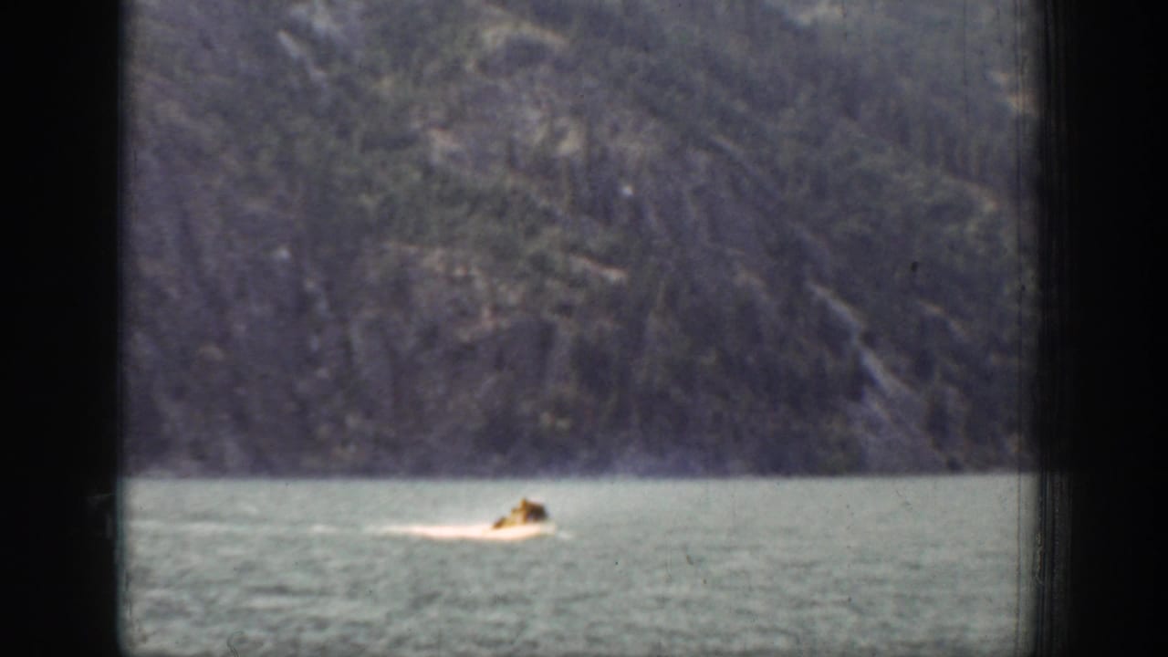 Small motorboat crossing a lake below forested mountain slopes.
