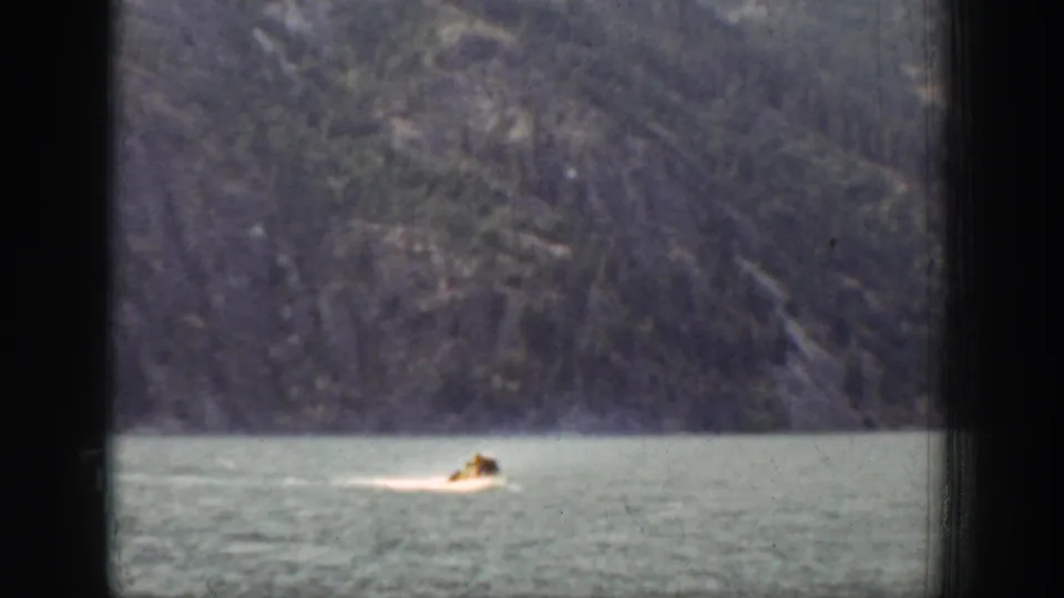 In supported 1939 Chelan, Washington footage, a small motorboat moves across calm lake water below steep mountains.