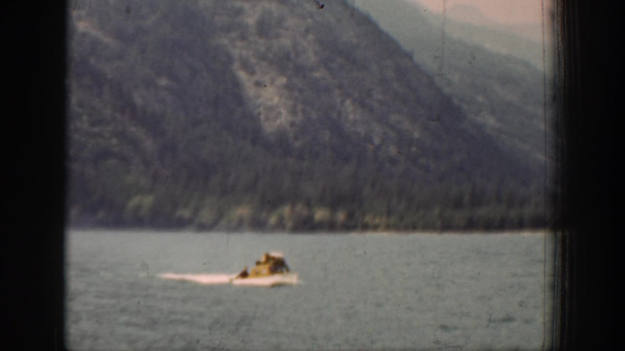 The 8mm frame shows a small motorboat and pale wake on a calm Chelan lake, seen through dark frame edges.
