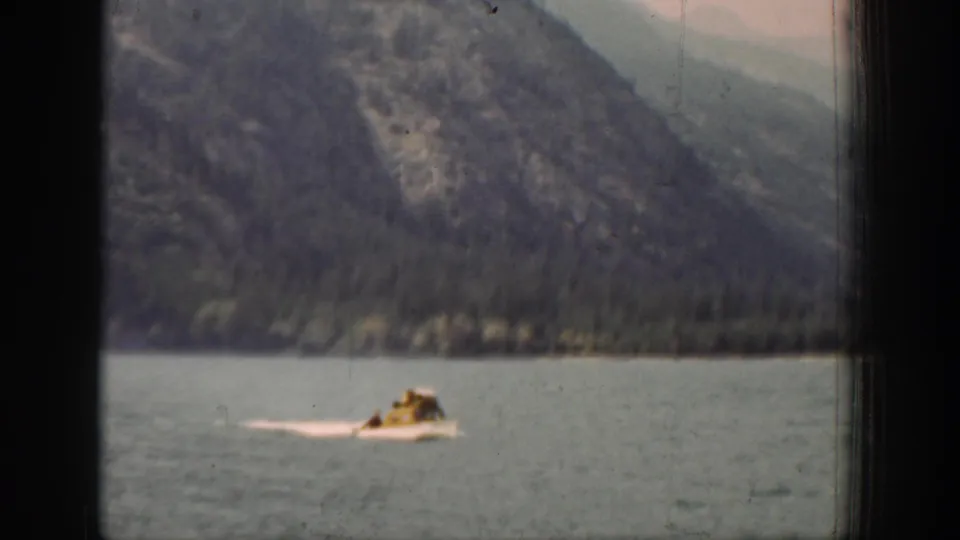 The 8mm frame shows a small motorboat and pale wake on a calm Chelan lake, seen through dark frame edges.