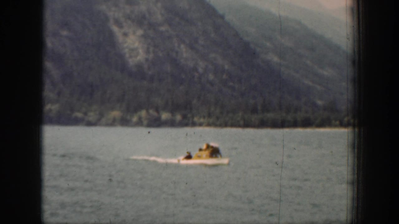 Small motorboat crossing a mountain lake with forested slopes in the background.