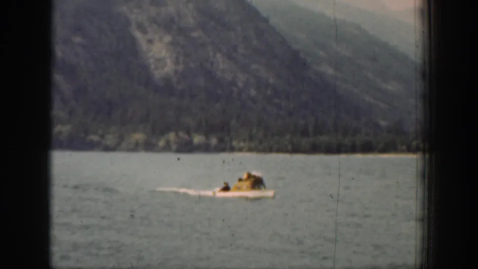 1939 Chelan, Washington home-movie frame showing a small motorboat moving across a broad lake below forested mountains.