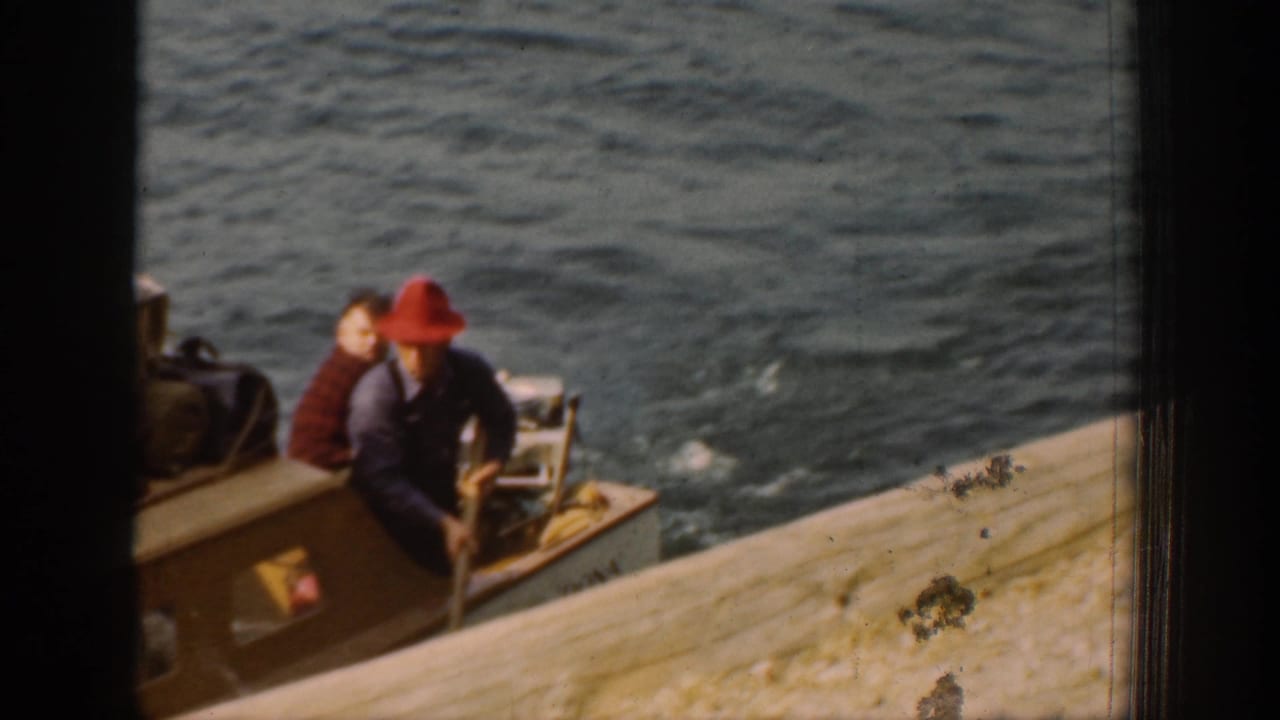 Close home-movie frame from Chelan showing two boat passengers beside the camera vessel, including one person wearing a red hat.