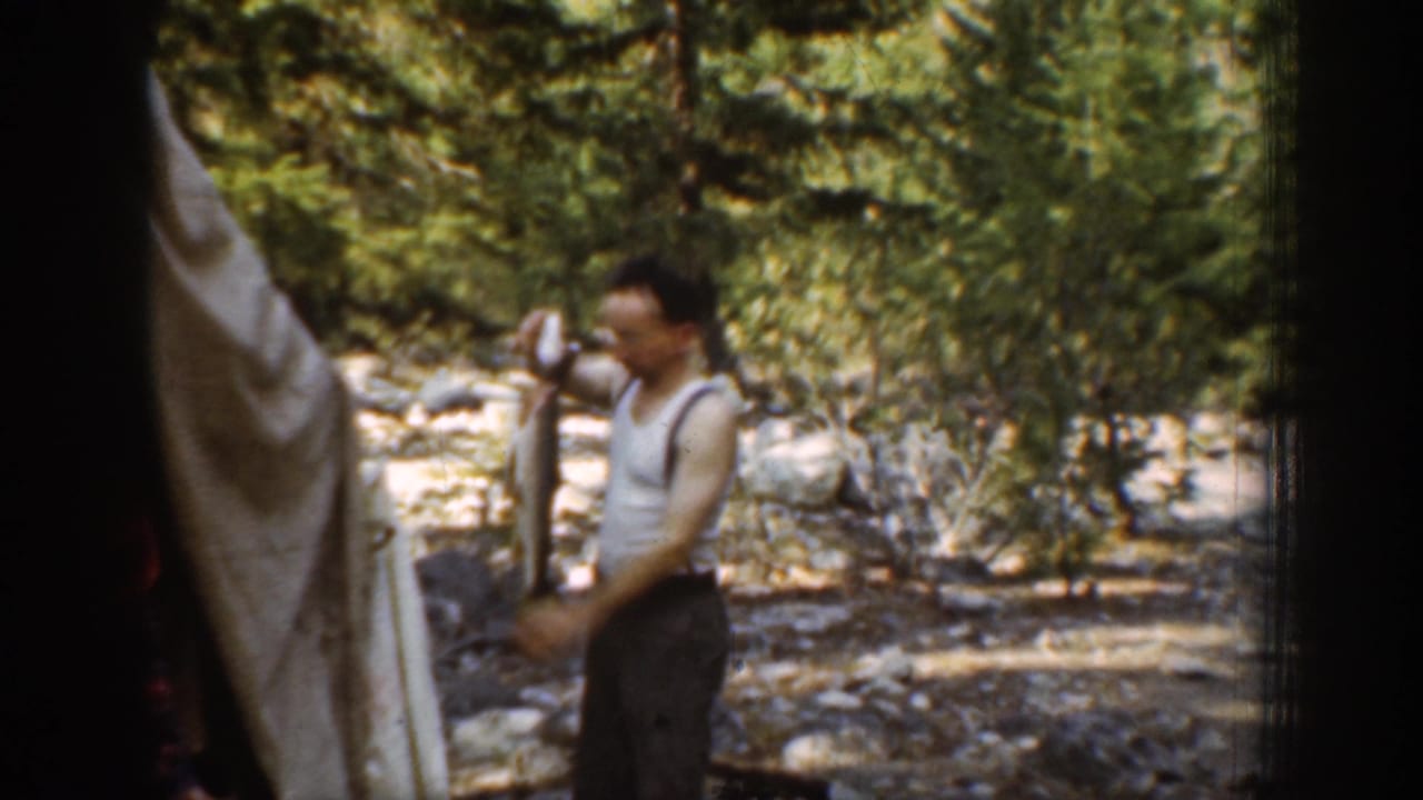 In Chelan, Washington 1939 home-movie footage, a man in suspenders holds a large fish beside a rocky forest stream.