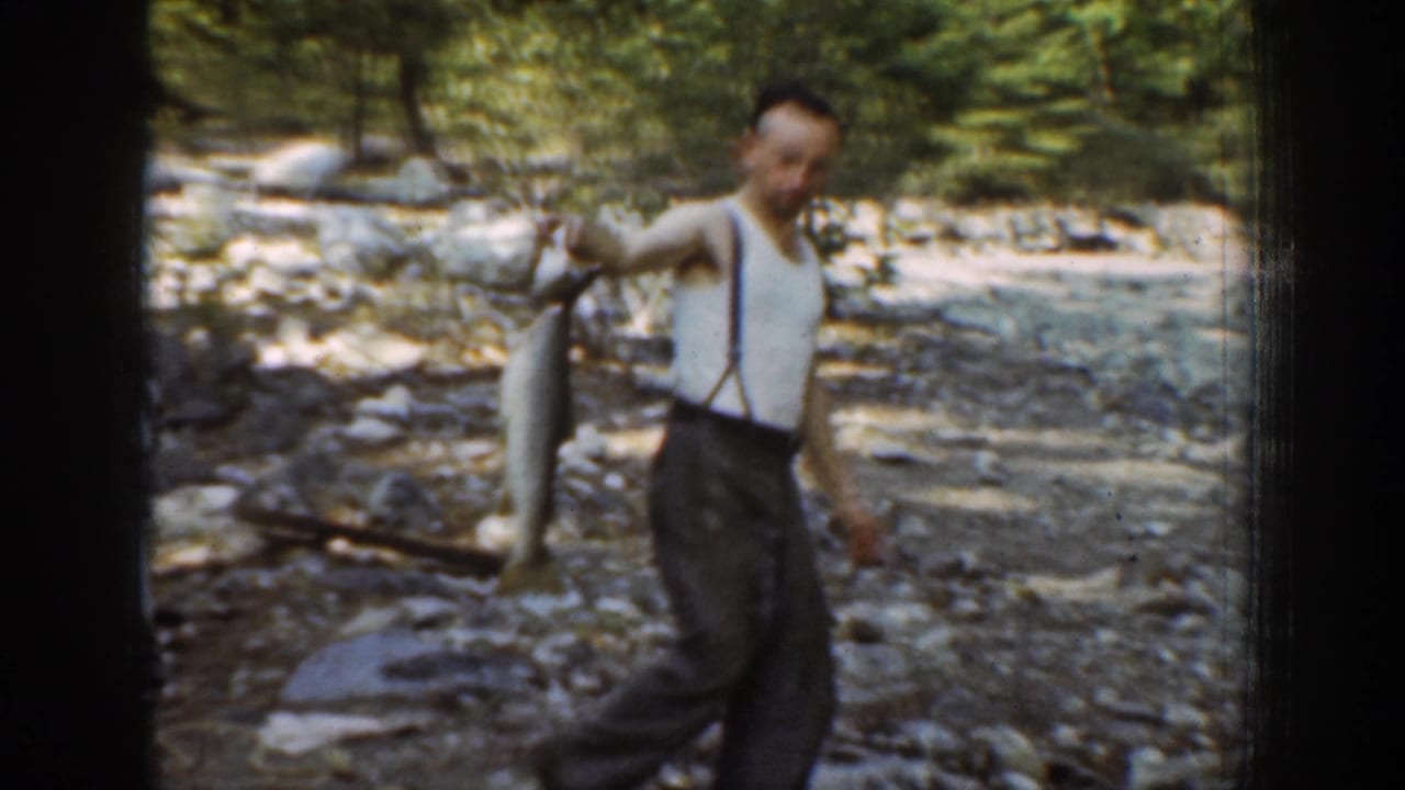 Man holds a large fish out to the side while standing in a rocky wooded stream area.