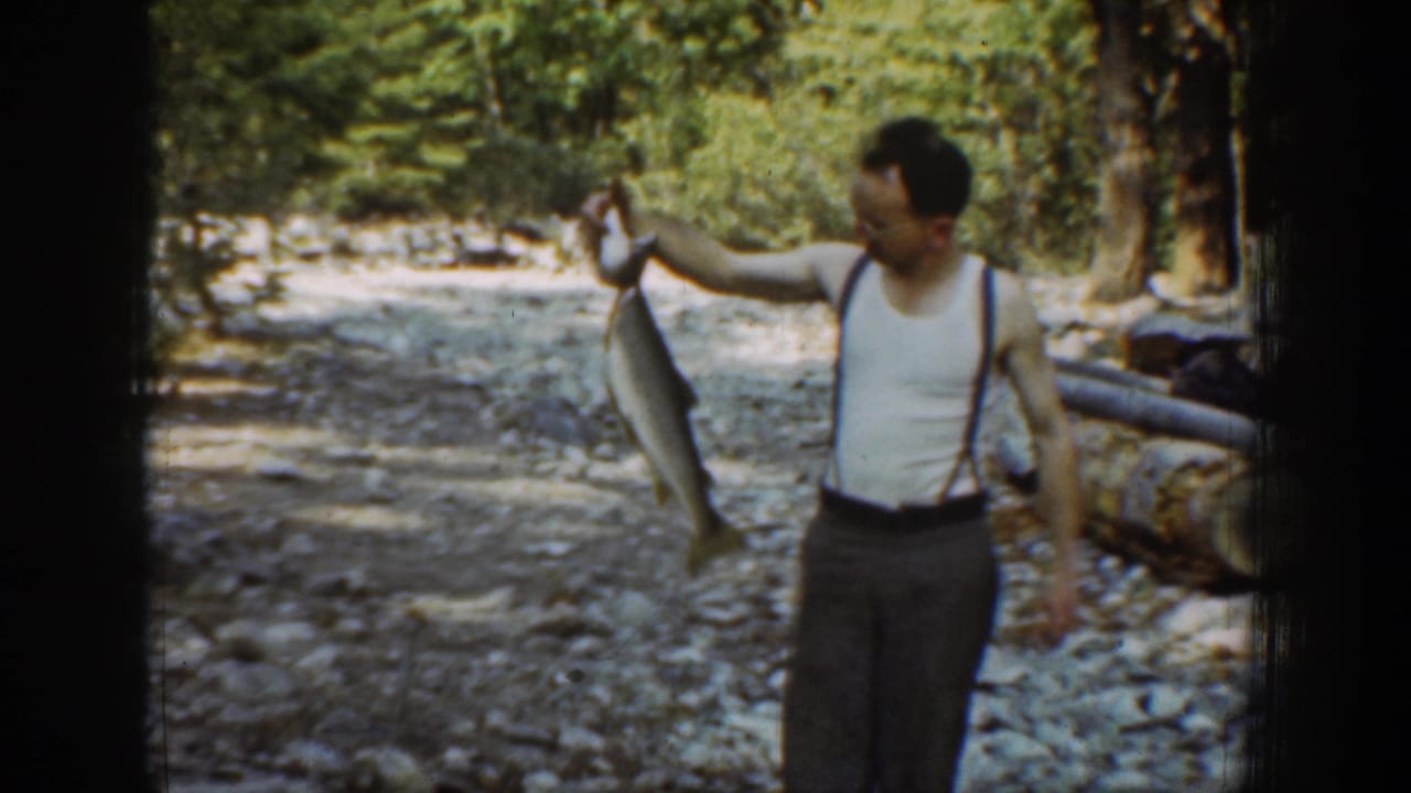 Chelan, Washington 1939 home-movie frame showing a man lifting a large fish near a wooded rocky stream.