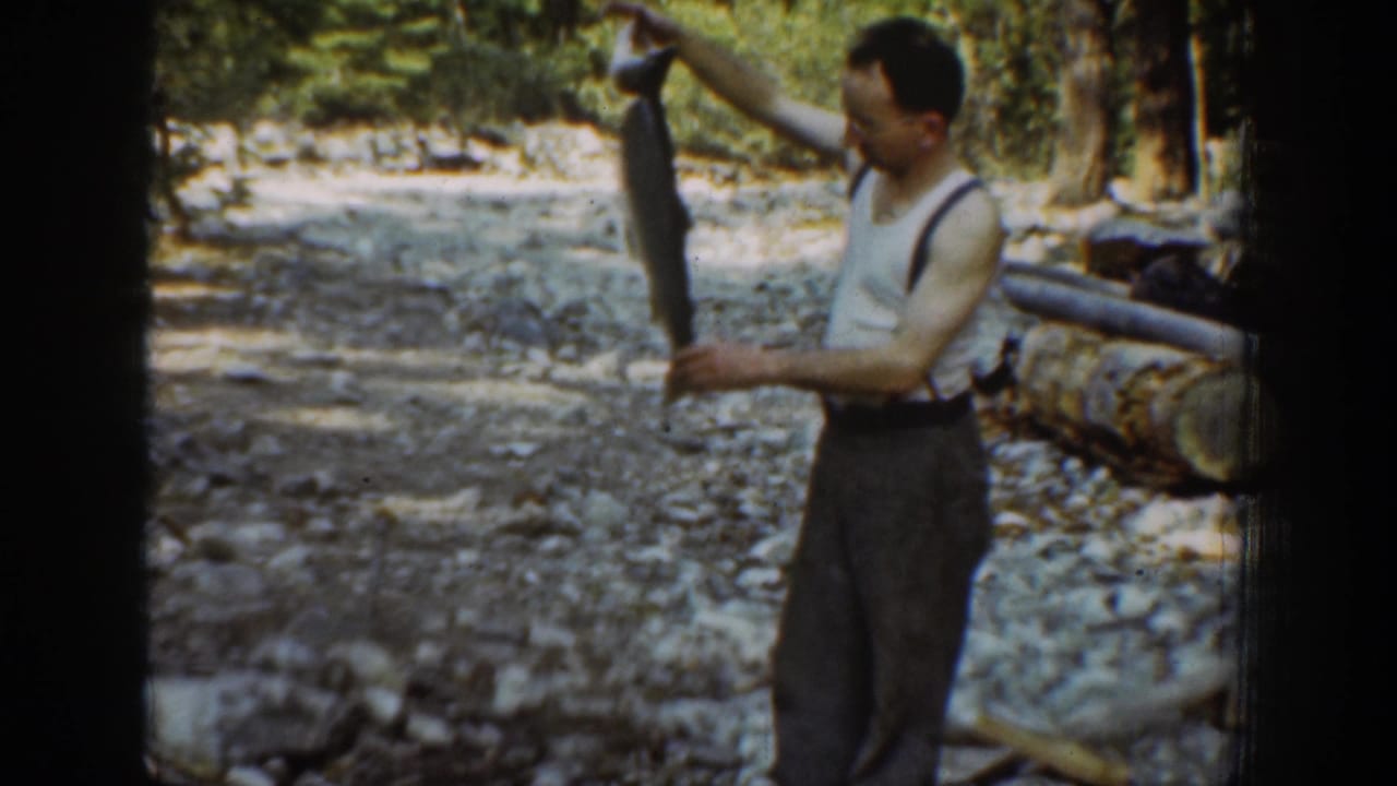 In the final frame, the man looks at the large fish he is holding near a log railing in Chelan, Washington footage from 1939.