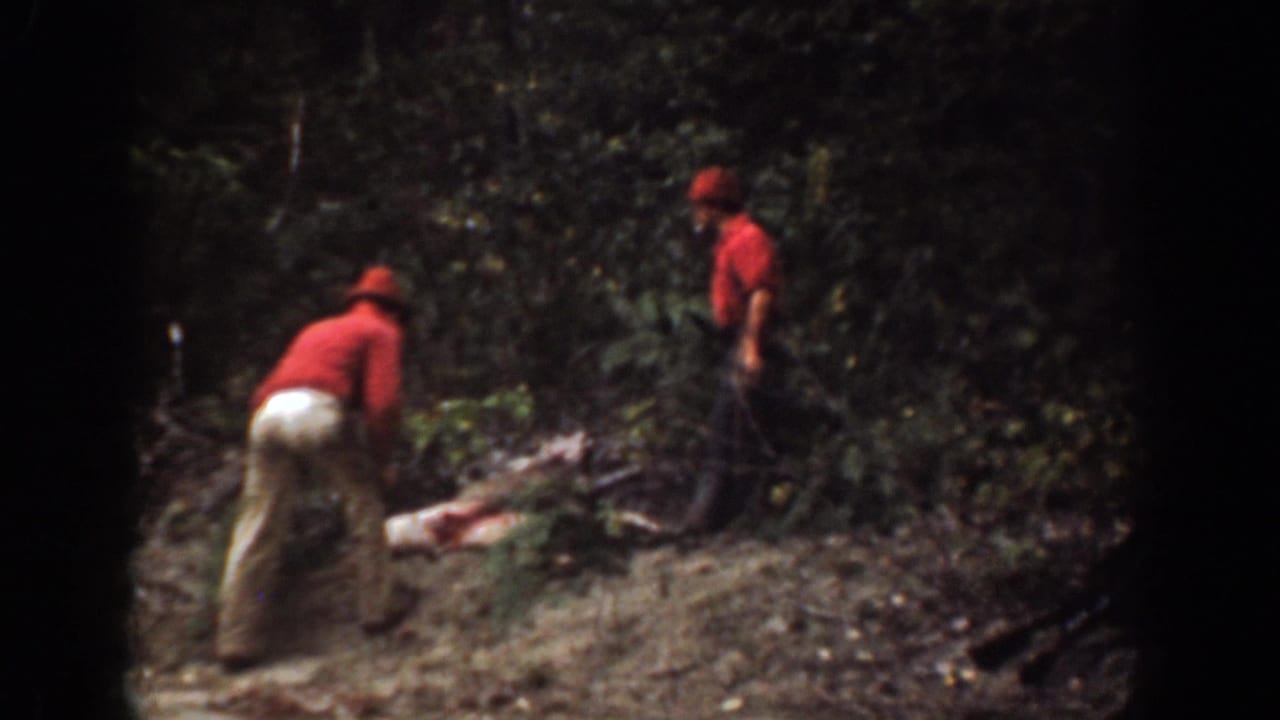 In 1939 Chelan, Washington home-movie footage, two adult men in red shirts and hats appear to handle a deer in a wooded clearing.