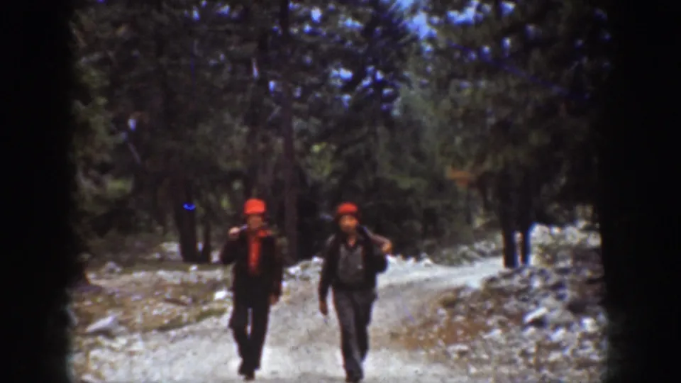 Two men in red hats walk down a dirt forest road in the 1939 Chelan, Washington home-movie footage.