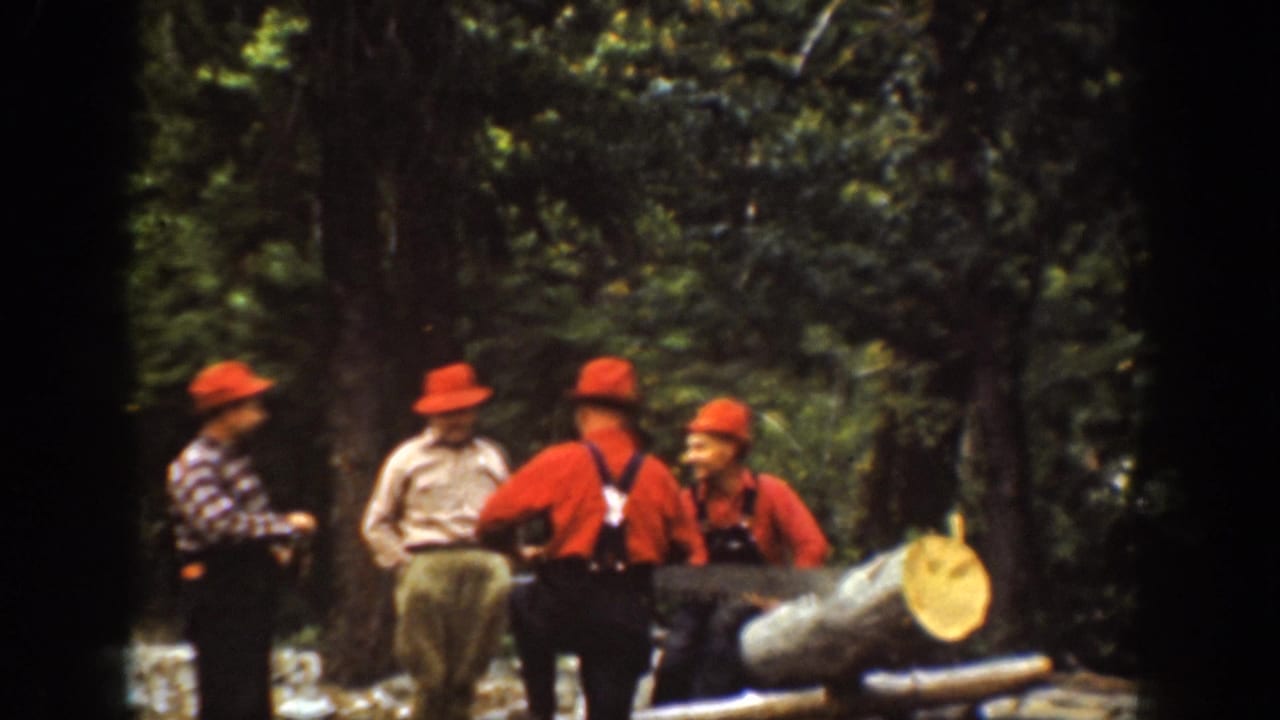 Men in red hats and work clothes stand around a felled tree trunk in the forest.