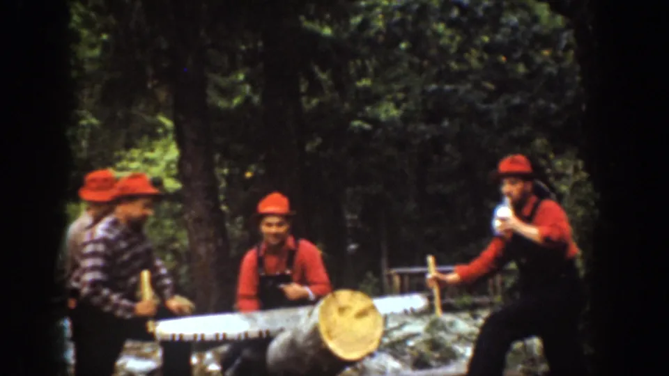 Chelan, Washington 1939 home-movie frame of four men in red hats gathered around a large log with a two-man crosscut saw.