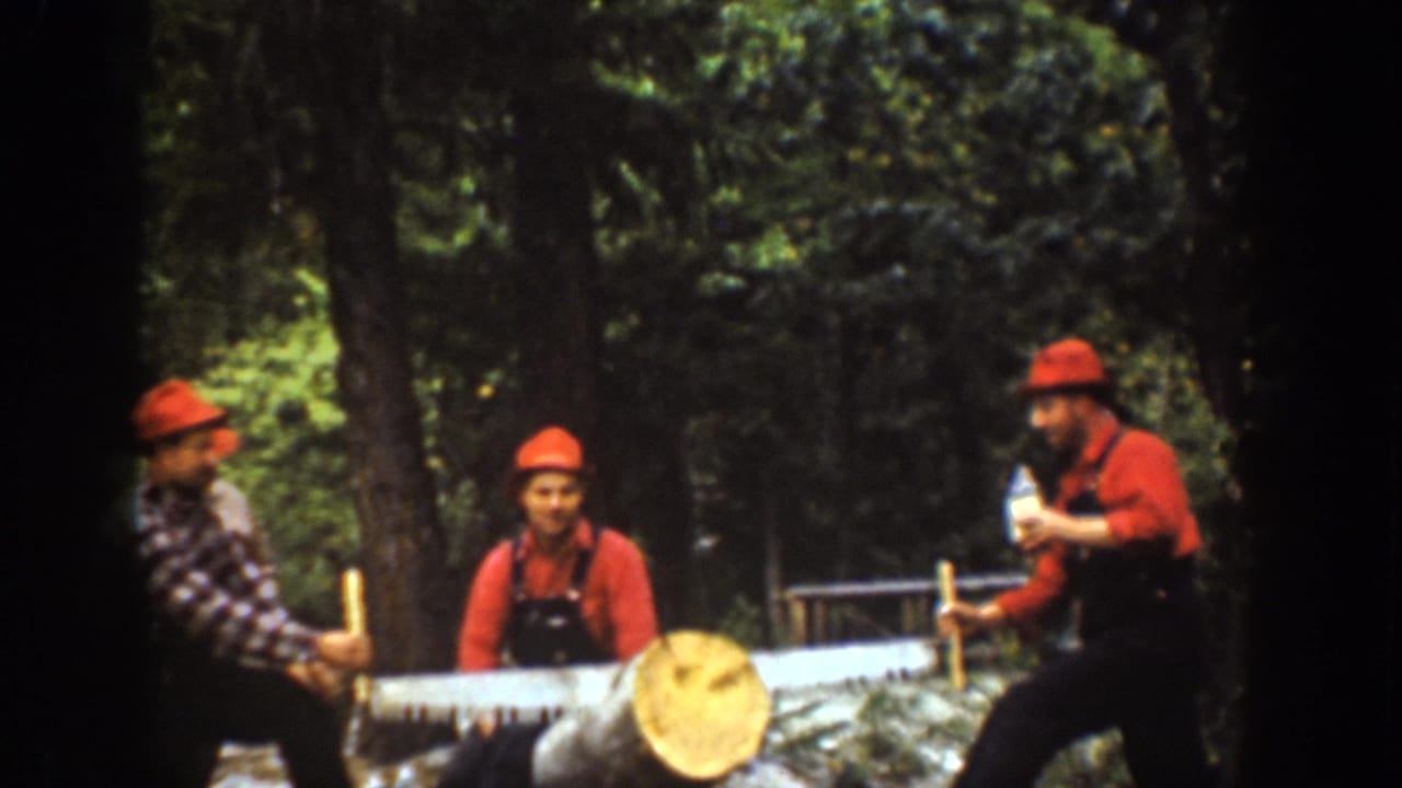Men in red hats hold a long saw across a log while one man drinks from a bottle.