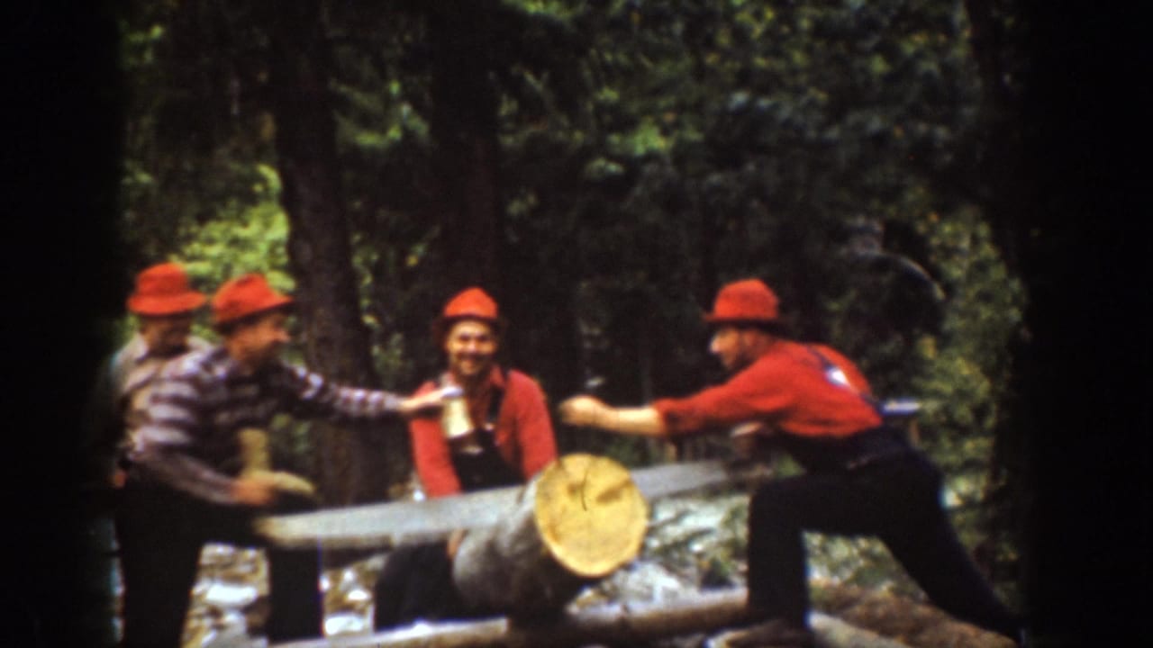 A man reaches across the log while another man offers a bottle near the saw.