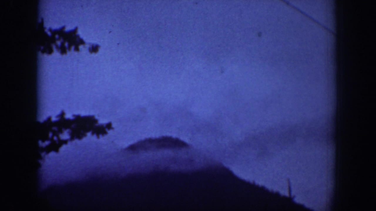 1939 Chelan-area 8mm frame showing a dark mountain shape, blue sky or haze, tree branches, and a diagonal utility line.