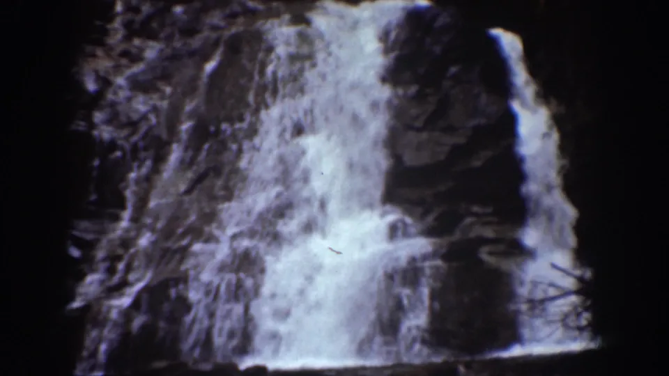 1939 Chelan, Washington frame showing a waterfall dropping over a rugged rock face with visible spray and dark borders.