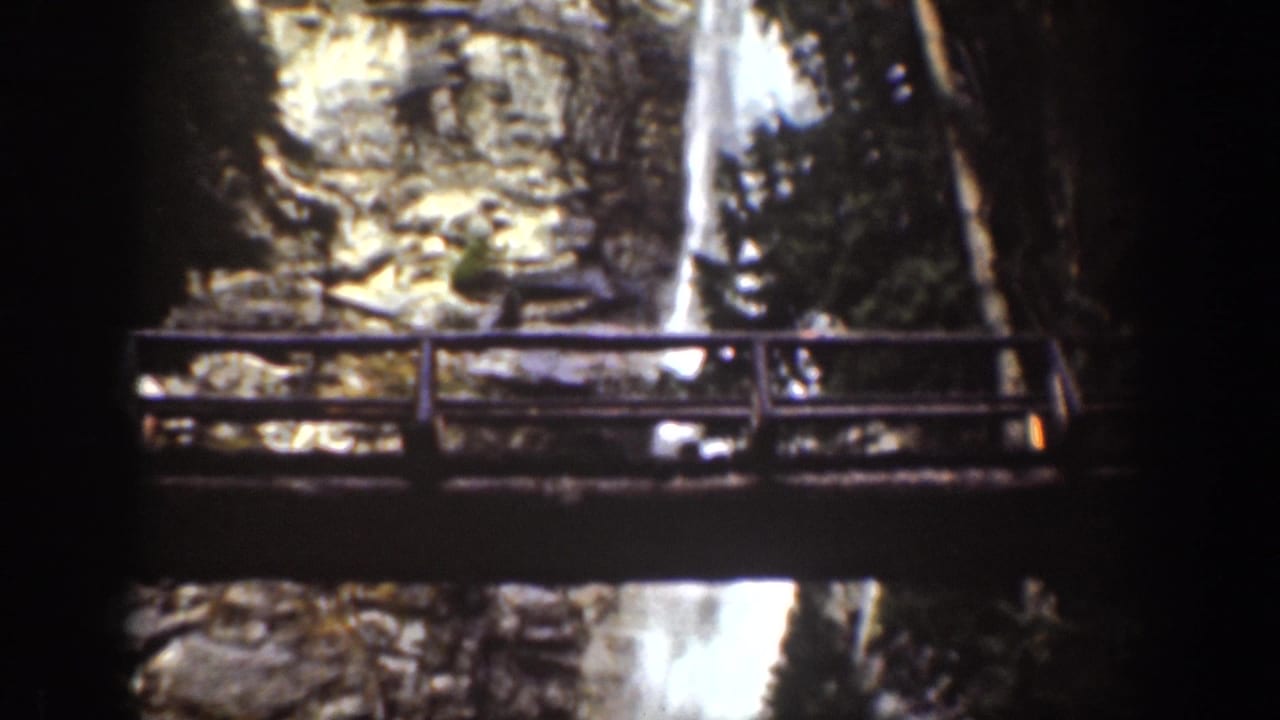 Wooden observation bridge crossing in front of a rocky waterfall gorge.