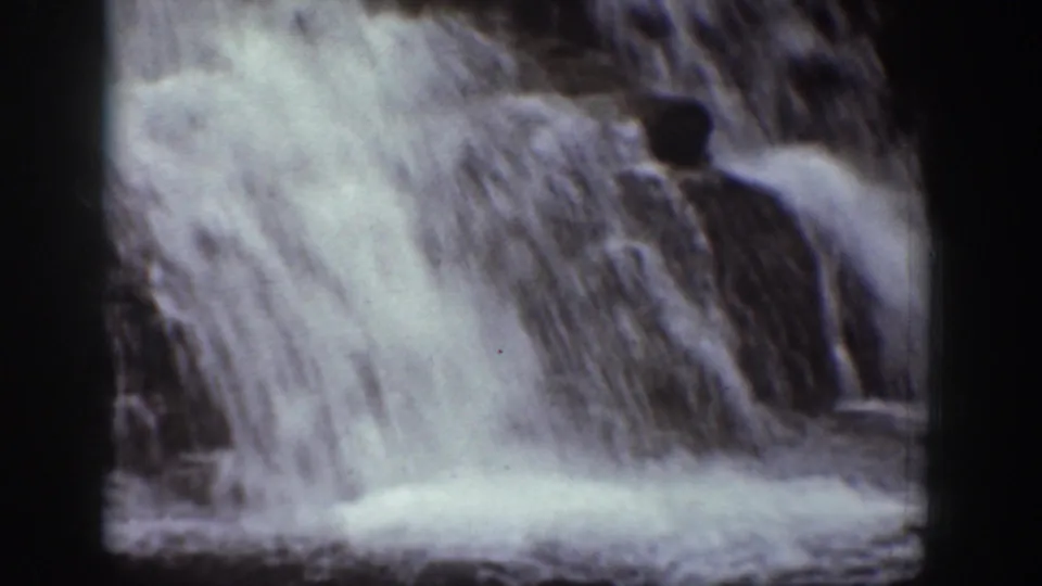 1939 Chelan, Washington home-movie frame showing rushing waterfall water over dark rocks in soft, grainy 8mm exposure.