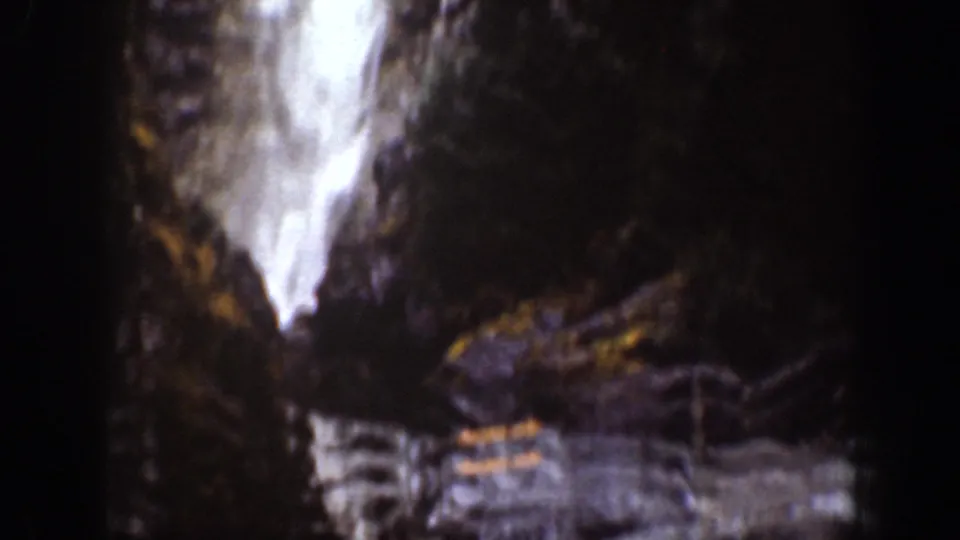 Grainy 1939 home-movie frame showing a waterfall dropping through a shadowed rocky area with surrounding vegetation.