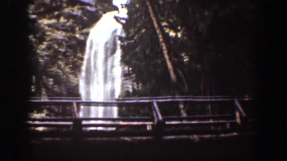 Wider Chelan, Washington waterfall view with a railing in the foreground and trees around the bright falling water.