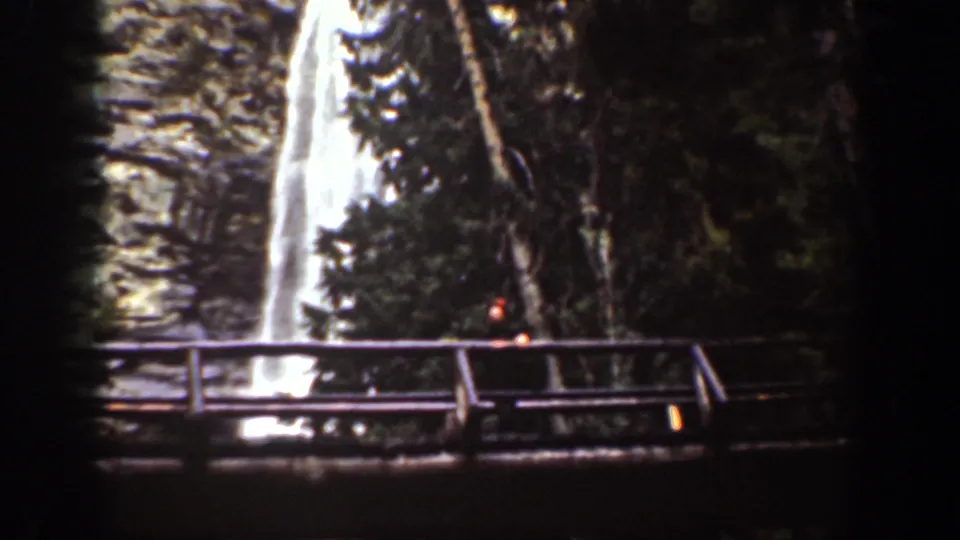 Chelan, Washington home-movie frame with a waterfall, forest trees, and a wooden viewing bridge in the foreground.