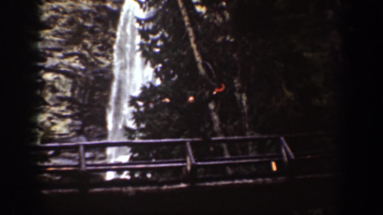 1939 Chelan, Washington home-movie frame showing a waterfall above a wooden bridge or railing in a shaded rocky gorge.